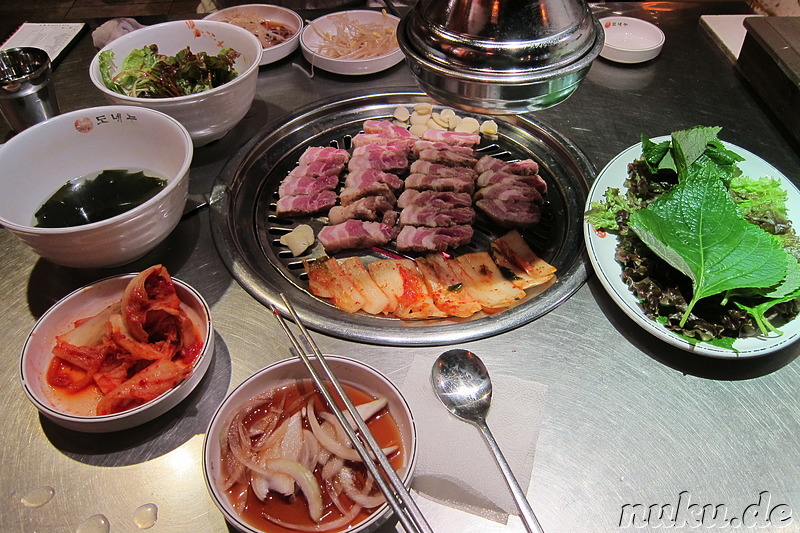 Am Tisch gegrilltes Schweinebauchfleisch (Samgyeobsal; 삼겹살), Kimchi u. Knoblauch