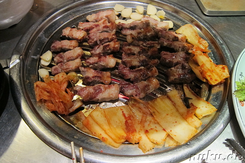 Am Tisch gegrilltes Schweinebauchfleisch (Samgyeobsal; 삼겹살), Kimchi u. Knoblauch